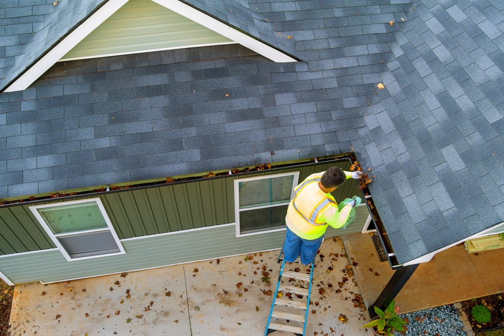 A worker is cleaning clogs in roof gutter drain by picking up dirt, debris, fallen leaves